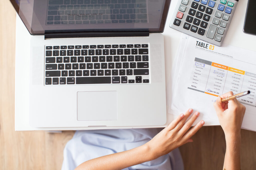 mãos da mulher de negócios fazendo anotações no documento com a mesa e trabalhando no computador portátil na mesa. Vista do topo