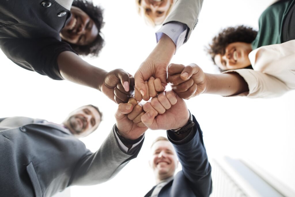 Engajamento dos colaboradores representado por equipe unindo os punhos em demonstração de colaboração, união, motivação e trabalho em equipe.